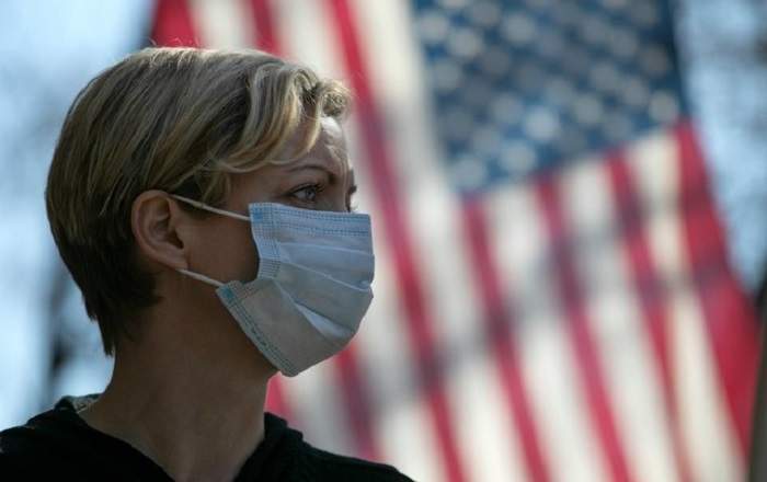 A woman wearing a mask with the US flag in the background. (File Photo, Image credit: USNews.com)
